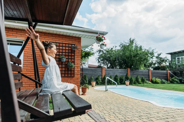 Side view of cute little kid with outstretched arms resting on wooden bench in summer day — Stock Photo