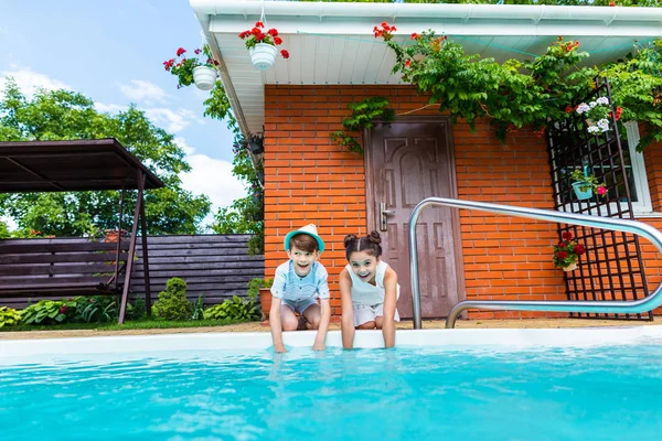 Fratelli piccoli seduti vicino alla piscina il giorno d'estate — Foto stock