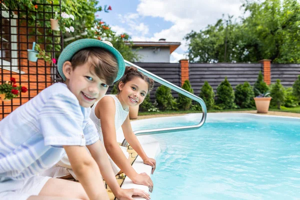 Vista laterale dei fratellini seduti vicino alla piscina durante la giornata estiva — Foto stock