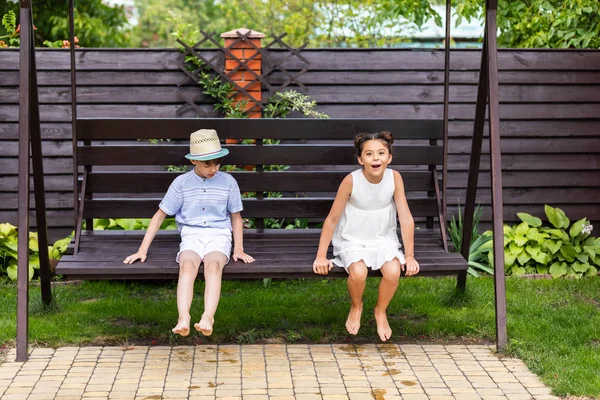 Mignons enfants assis sur un banc en bois ensemble sur la cour arrière le jour d'été — Photo de stock