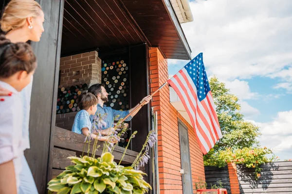 Famille avec drapeau américain debout sur le porche de la maison de campagne — Photo de stock
