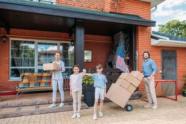 Crianças com chaves e pais com caixas de papelão em pé na casa de campo, movendo-se para casa conceito — Fotografia de Stock