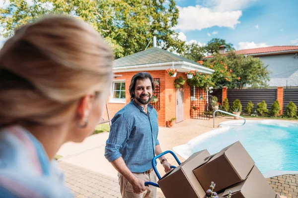 Smiling man with handle tray with cardboard boxes looking at wife on porch of new house, moving home concept — Stock Photo