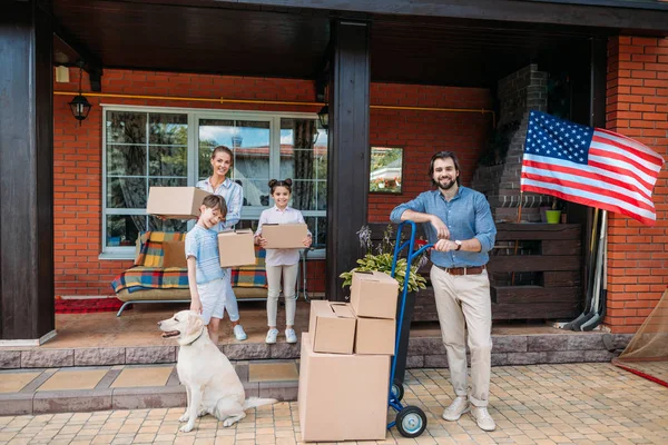 Семья с картонными коробками и лабрадором собака, стоящая на крыльце загородного дома, движущаяся концепция дома — стоковое фото