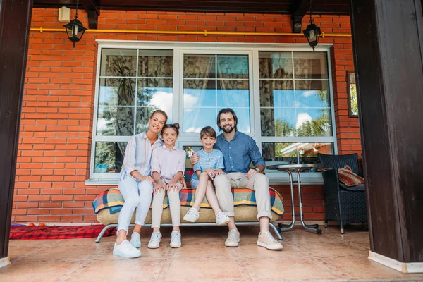 Lächelnde Familie sitzt zusammen auf dem Sofa auf der Veranda des Landhauses — Stockfoto