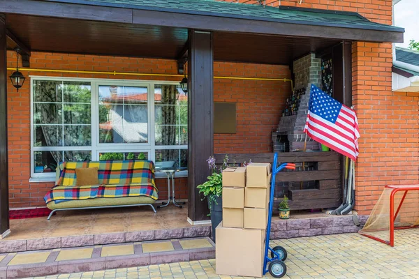 Hand truck with cardboard boxes and sofa on porch of country house — Stock Photo