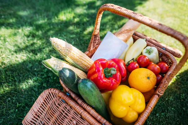 Vista de cerca de la cesta con bolsita y verduras para picnic sobre hierba verde - foto de stock