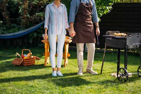 Teilansicht des Paares, das Händchen hält, während es beim Grillen im Hinterhof steht — Stockfoto