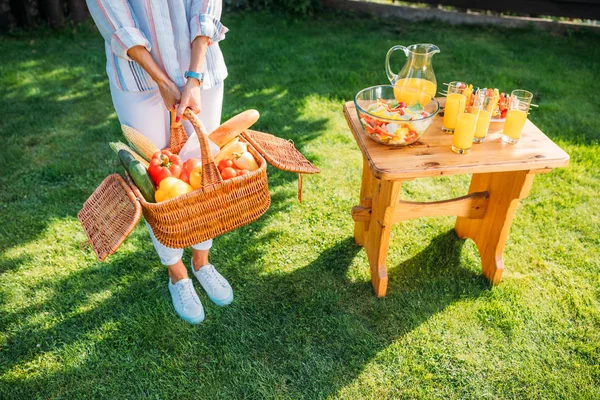 Colpo ritagliato di donna con cesto pieno di verdure fresche per picnic sul cortile — Foto stock