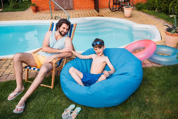 Lächelnder Vater und Sohn ruhen sich an einem Sommertag in der Nähe des Swimmingpools im Hinterhof aus — Stockfoto