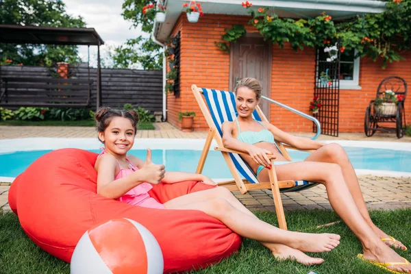 Madre e figlia sorridente che riposa vicino alla piscina sul cortile il giorno d'estate — Foto stock