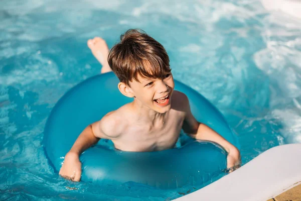 Portrait of happy boy with inflatable ring swimming in swimming pool on summer day — Stock Photo