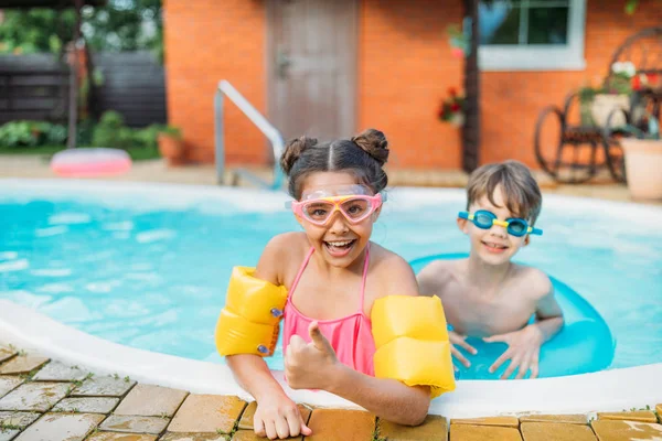 Petits frères et sœurs nageant dans la piscine ensemble le jour de l'été — Photo de stock