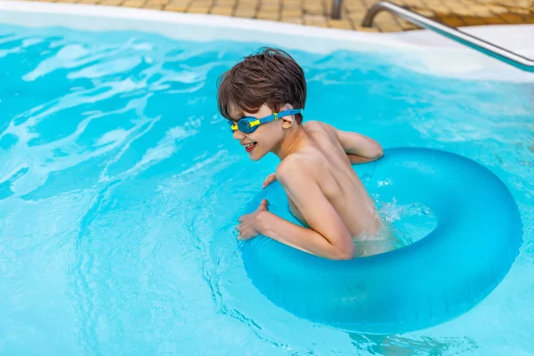Vista laterale del ragazzo felice in occhiali da bagno con anello gonfiabile che nuota in piscina durante la giornata estiva — Foto stock