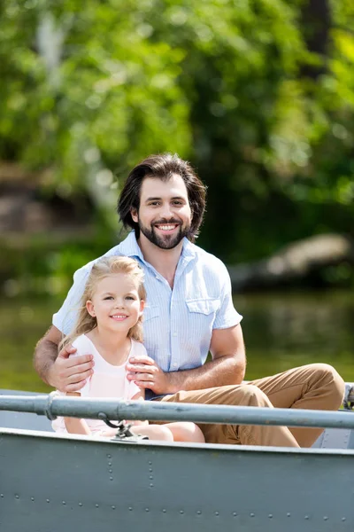 Happy father and daughter sitting in boat on lake at park and looking at camera — Stock Photo