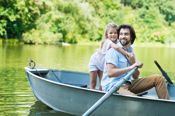 Figlia felice abbracciando il padre da dietro mentre cavalcano in barca sul lago al parco — Foto stock