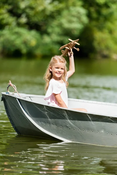 Beautiful little child playing with toy plane floating in boat on lake — Stock Photo