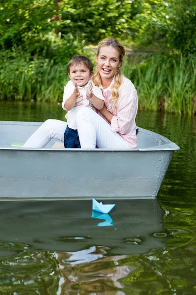 Mère heureuse avec fils équitation bateau sur le lac au parc et applaudissements mains — Photo de stock