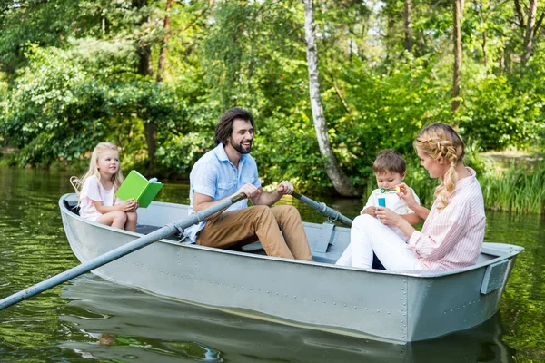 Lächelnde junge Familie reitet Boot auf Fluss im Park — Stockfoto