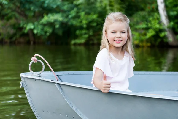 Beautiful little child showing thumb up at camera while floating in boat on lake — Stock Photo