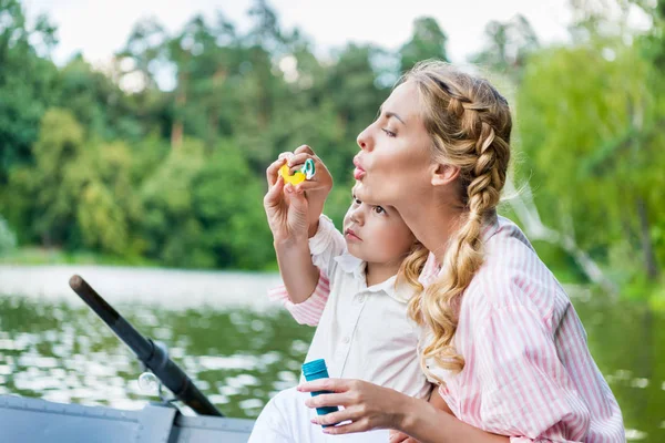 Mère heureuse avec fils soufflant des bulles de savon tout en chevauchant bateau au parc — Photo de stock