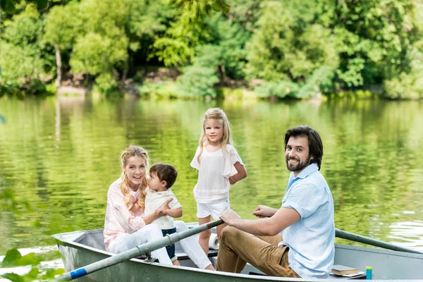 Happy young family riding boat on lake at park and looking at camera — Stock Photo