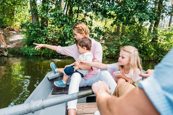 Beautiful young family riding boat on lake and pointing somewhere at park — Stock Photo