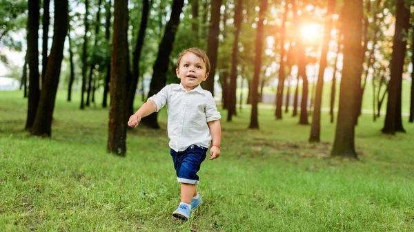 Cute little kid in white shirt and denim shorts running by park — Stock Photo