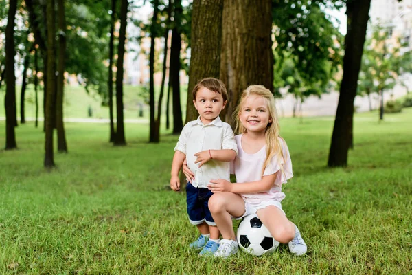 Hermanito y hermana con pelota de fútbol abrazándose en el parque - foto de stock