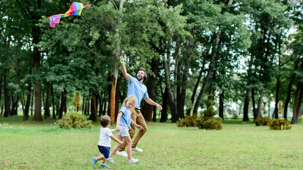 Vista lateral del padre guapo y los niños jugando con cometa en el parque - foto de stock