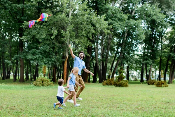 Vista lateral de feliz padre y niños jugando con cometa en el parque - foto de stock