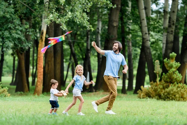 Seitenansicht des glücklichen Vaters und seiner Kinder beim Spielen mit dem Drachen im Park — Stockfoto