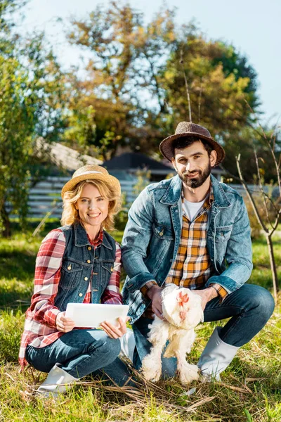 Granjero sosteniendo pollo mientras su novia usando tableta digital cerca en rancho - foto de stock