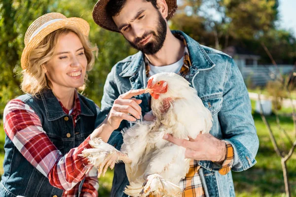 Улыбающаяся пара фермеров в соломенных шляпах с курицей на ферме — стоковое фото