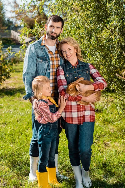 Farmer family with little daughter and brown rabbit outdoors — Stock Photo