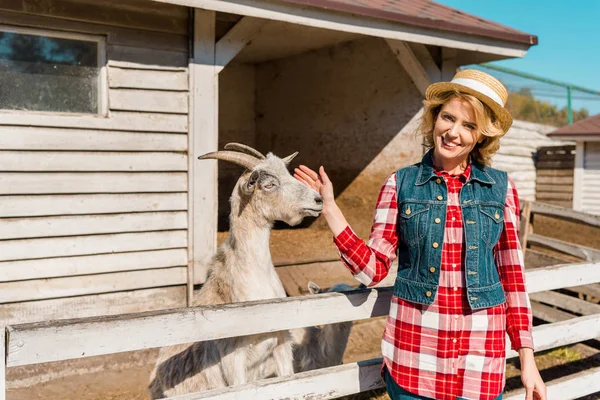 Erwachsene Bäuerin berührt Ziege in der Nähe von Holzzaun auf Ranch — Stockfoto