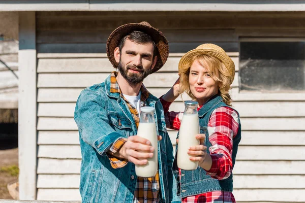 Adult couple of farmers in straw hats showing bottles of milk at ranch — Stock Photo
