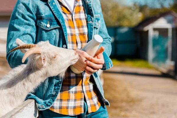 Image recadrée d'un agriculteur mâle avec bouteille de lait et de chèvre debout près d'une clôture en bois à la ferme — Photo de stock