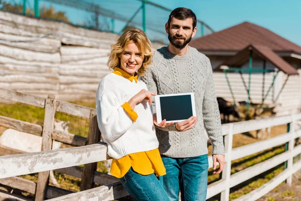 Adult couple of farmers showing digital tablet with blank screen near wooden fence at farm — Stock Photo