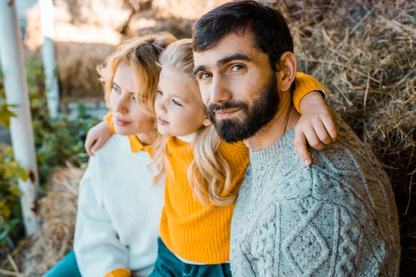 Adulto macho agricultor mirando cámara mientras su familia sentado detrás en granja - foto de stock