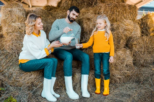 Adulto maschio contadino versando latte a piccola figlia mentre sua moglie seduta vicino al ranch — Foto stock