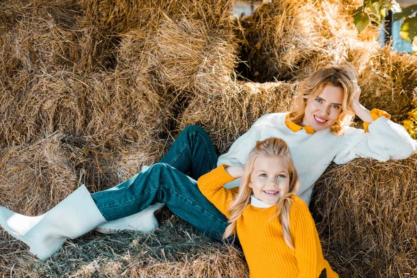 Lächelnde schöne Frau posiert mit kleiner Tochter auf Heuhaufen auf Bauernhof — Stockfoto