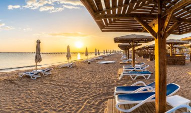 Landscape with sunbeds and umbrella on the Red Sea beach at sunrise in Hurghada, Egypt clipart