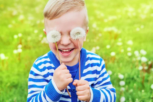 Mutlu çocuk gülüyor. Portre sevinç çocuk kadar kapatın. Göz gözlük olarak üzerinde oynak bir gülümseyen holding dandelions küçük şirin çocuk. Neşeli çocukluk, komik yaz günü, açık havada. Duygu yüz. Arka plan yeşil çimen