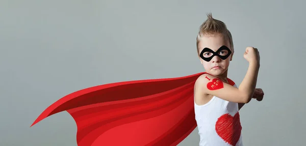 Funny strong child raising hand in success gesture. Little cool boy superhero loves mom, shows heart. Portrait confident kid in costume superman expresses strength, leadership. banner, copy space.