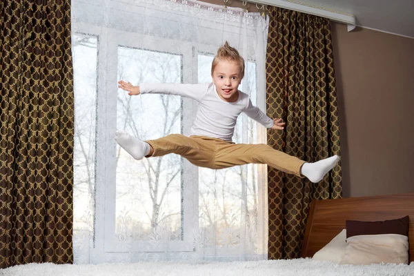 Dětské zábavné domů. Veselý kluk skákání v ložnici na posteli. Malé dítě 6 let šťastně hraje ráno v pokoji. zlomyslný dětství. — Stock fotografie