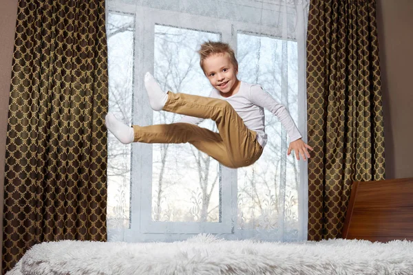 Dětské zábavné domů. Krásné blond dítě 6 let blbnout ráno do pokoje. Dítě s úsměvem, skákání na posteli do ložnice. — Stock fotografie