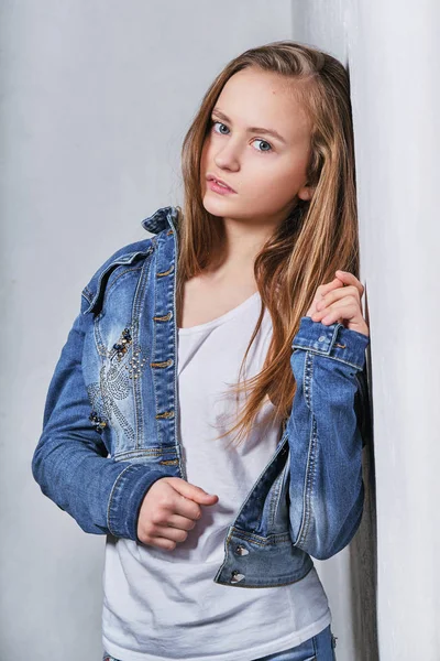 Moda portre kız beyaz duvarının yakınında. Şık güzel genç modeli kentsel rahat kıyafetler, kot ceket giydirdi. Kız sarışın ergen 11 yaşındaki kendine güvenen, ciddi yüz arıyorum poz. Model testleri.