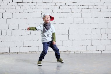 çocuk çocuk müzik dans. Cool çocuk hip hop. Şirin moda yaramaz çocuk. Rapçi ufaklık şapkası, spor ayakkabı, pantolon, tişört, sokak stili kıyafetler giyer. Stüdyo, tuğla duvar arka plan.