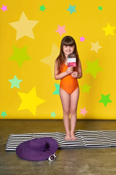 Moda verano niña, fondo brillante, estrellas, estudio. Un niño encantador en traje de baño sosteniendo helado. Pequeña morena modelo niño sonriendo posando. Concepto de vacaciones, calor, viajes, verano, playa, descanso . — Foto de Stock